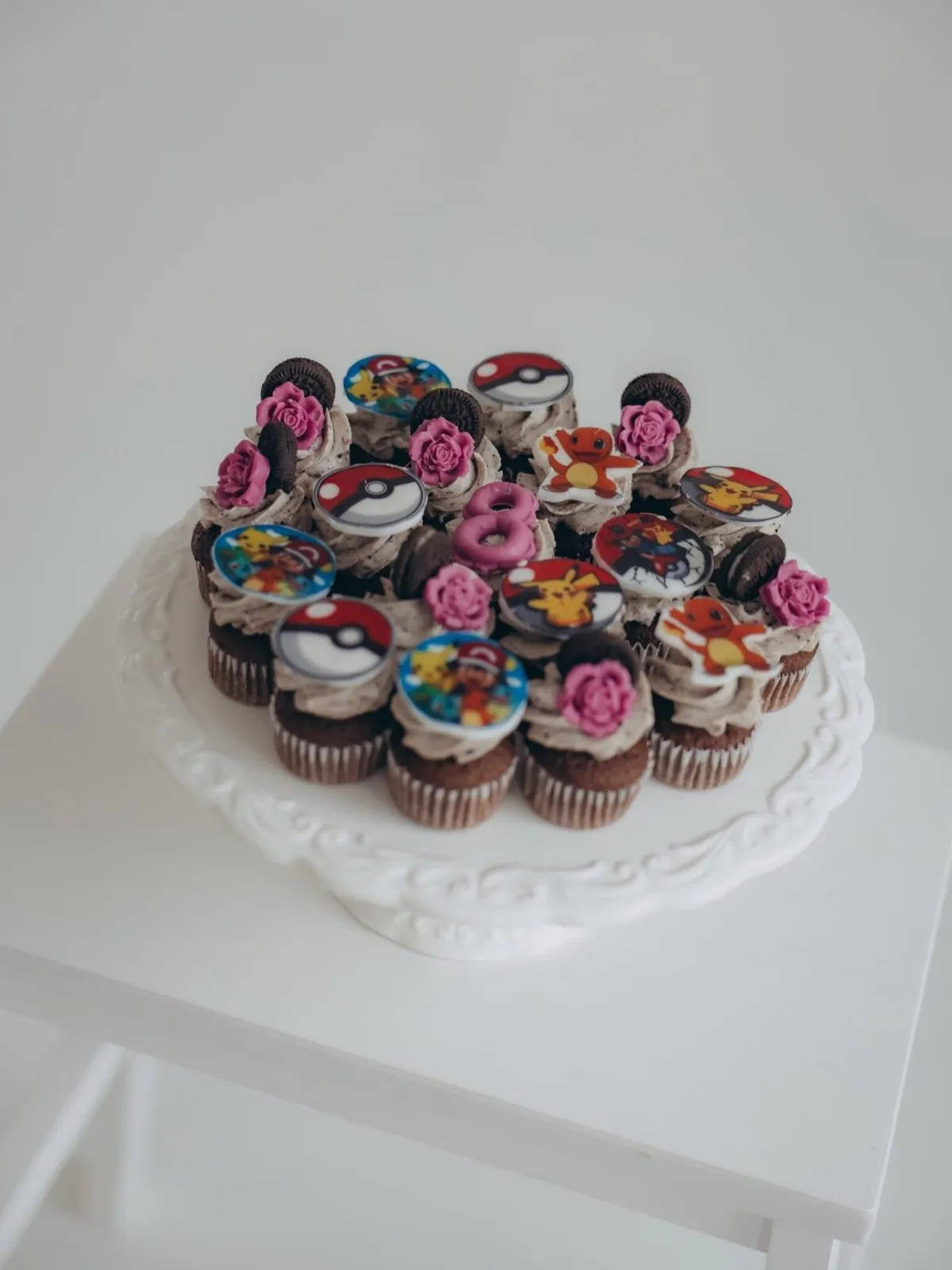 Mini šokolādes kēksiņi ar oreo krēmu, rozā rozītēm un krāsainiem rotājumiem uz balta statīva